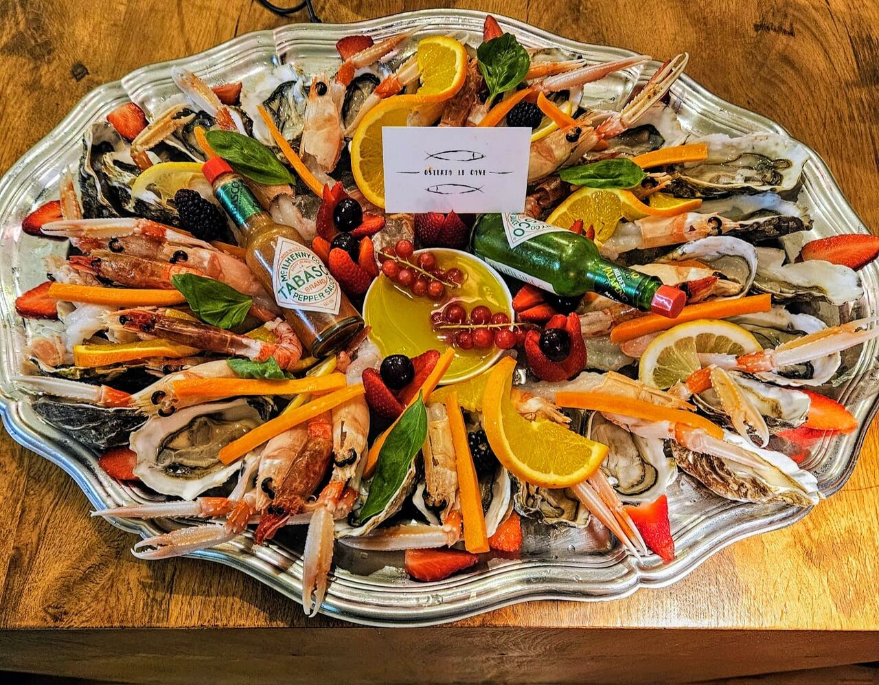 Tagliere di crudo di mare con gamberi, ostriche e frutti rossi, servito su vassoio d'argento
